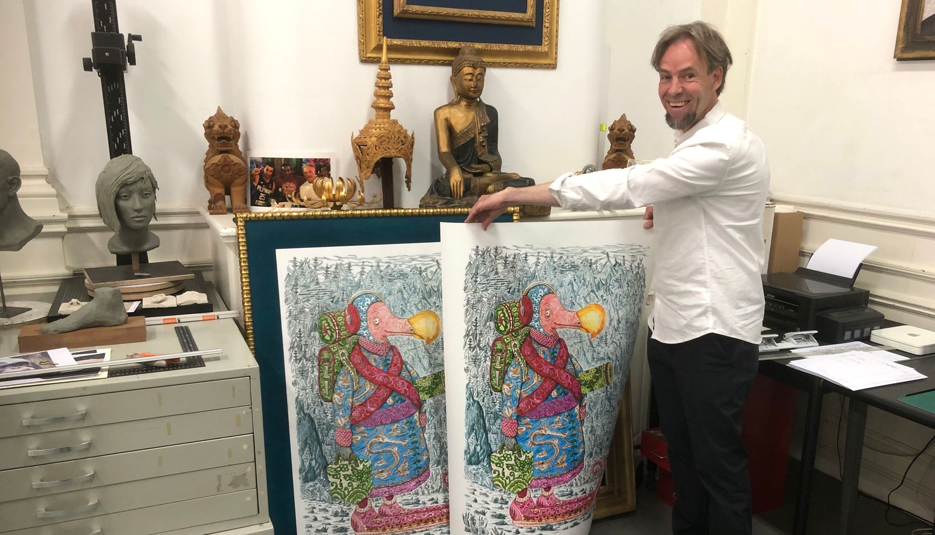 Een man staat naast twee kleurrijke abstracte schilderijen in een kamer vol kunst.