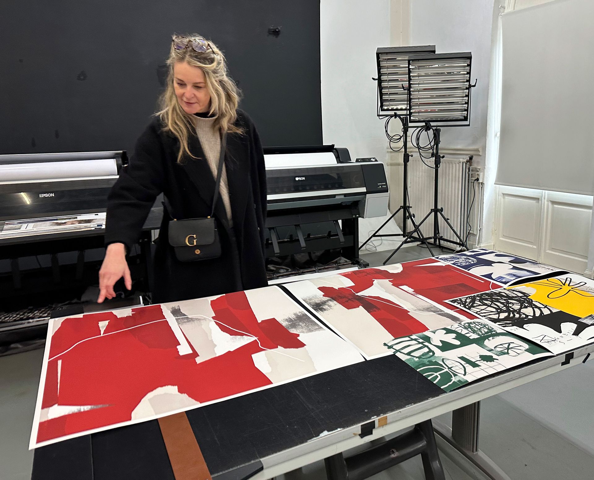 Een vrouw bekijkt een groot abstract kunstwerk in de kleuren rood, wit, zwart en groen, dat op een tafel in een atelier staat.