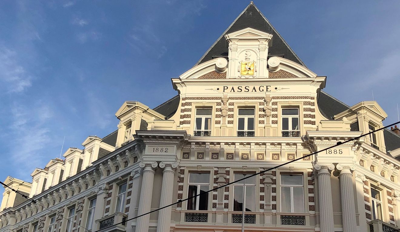 Een sierlijk wit historisch gebouw met een steil donker dak onder een blauwe hemel, gezien vanaf beneden.