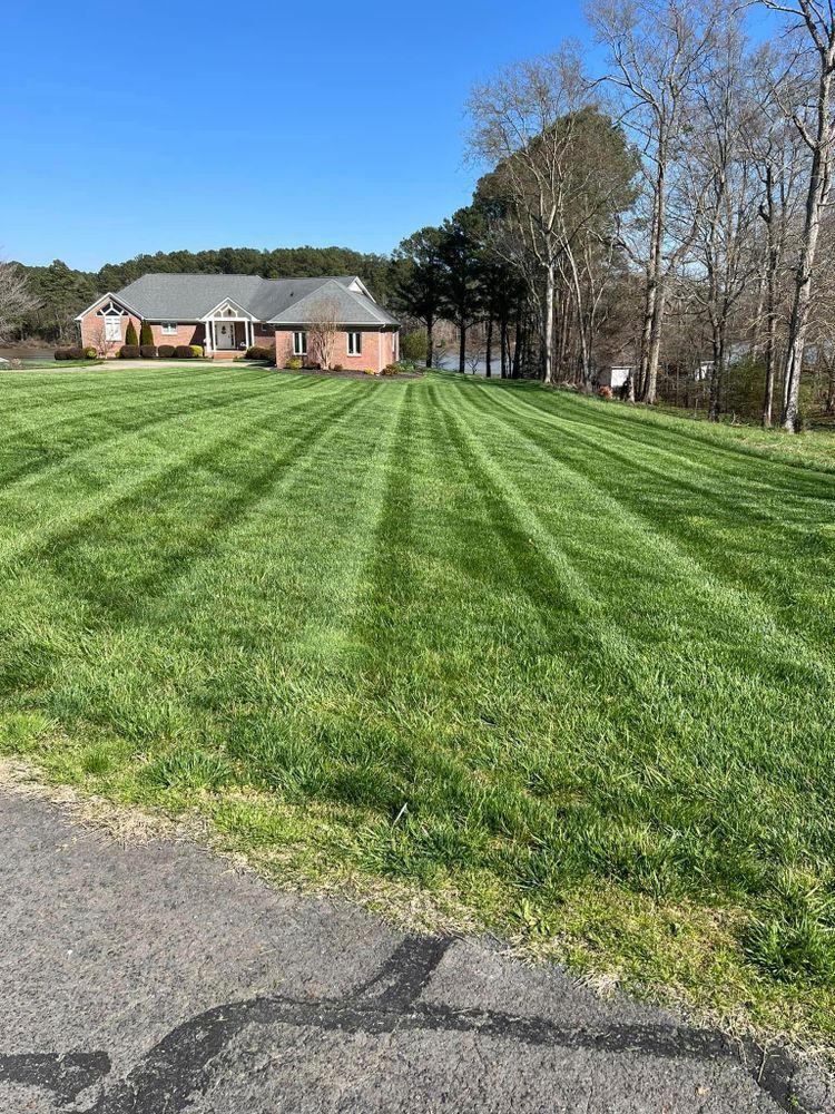 Lawn with fresh mowing stripes in front of a brick house. Trees and water in the background, blue sky.