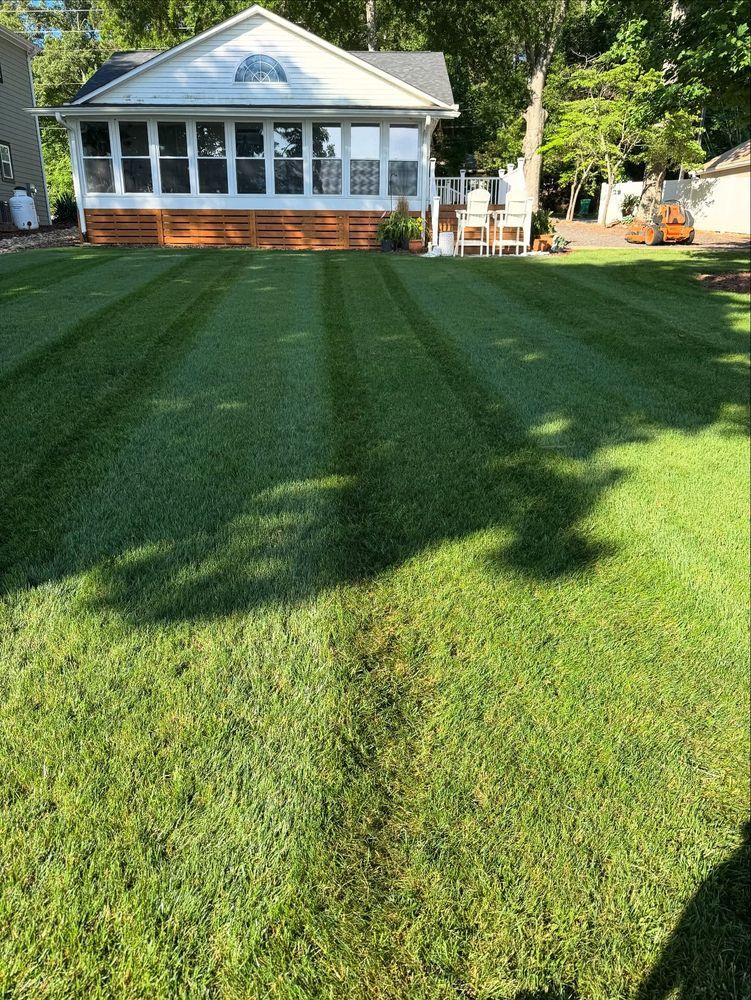 Green lawn with freshly cut stripes in front of a white house with a screened porch.