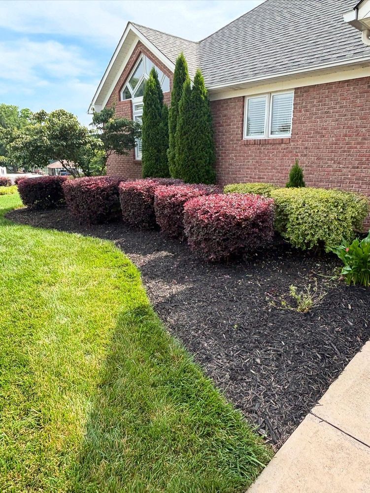 Red shrubs and green grass border a brick building with a curved roof.