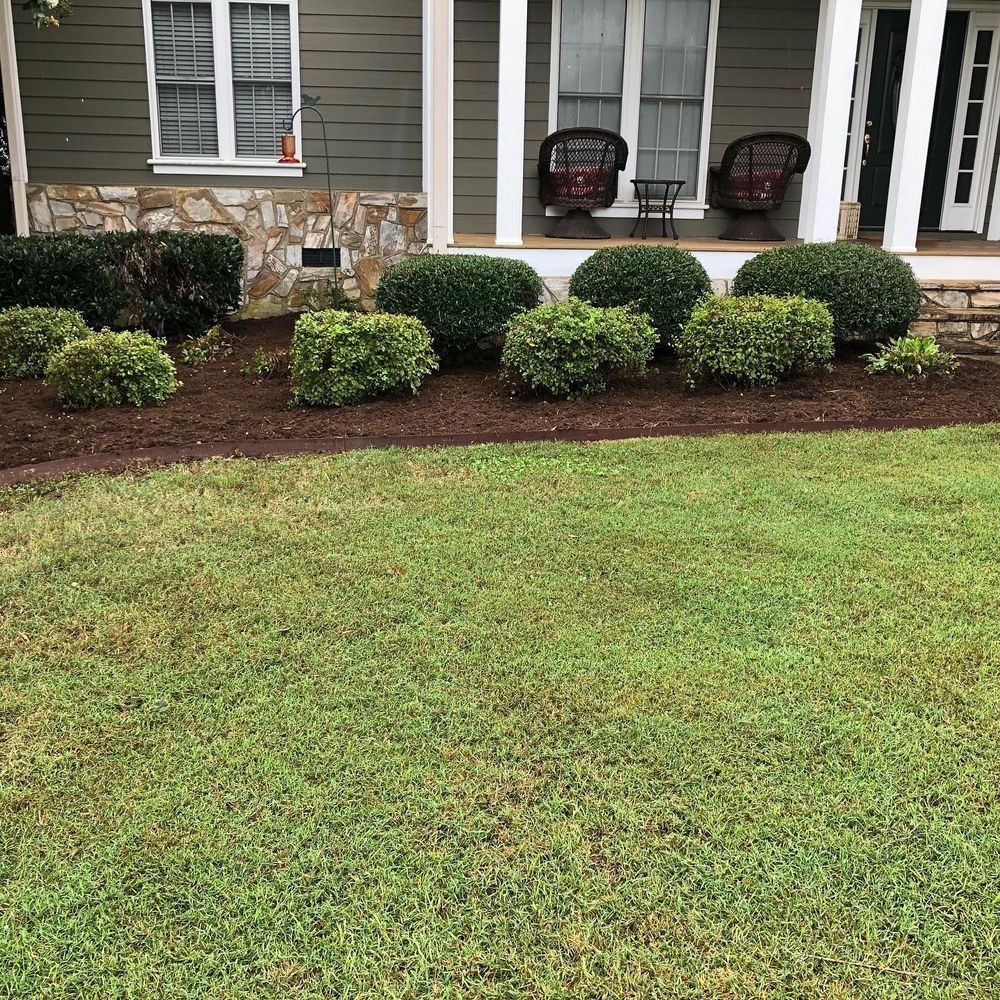 Front yard with green lawn, shrubs, and house with porch.