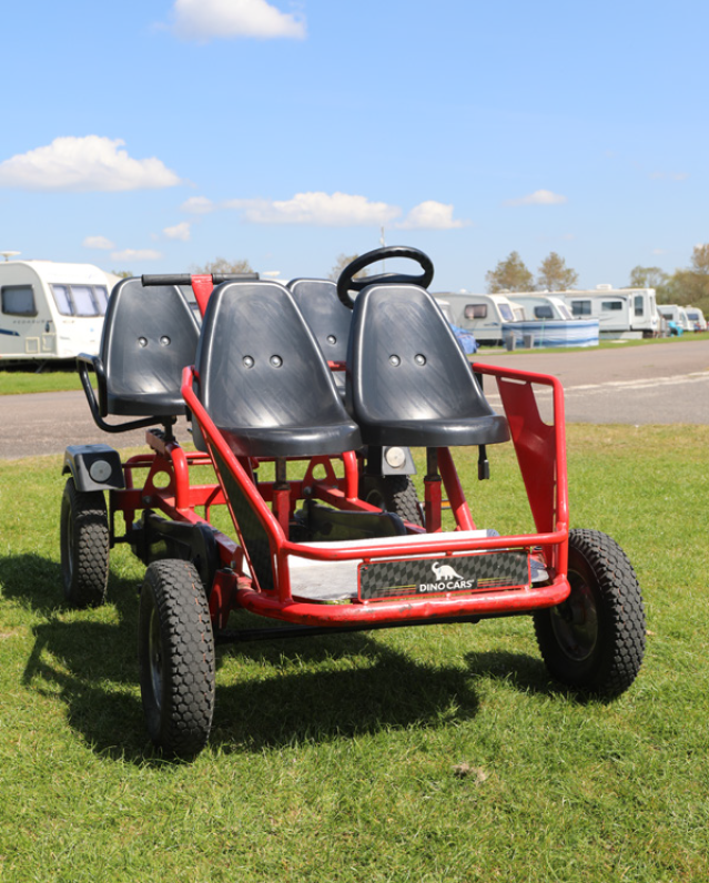 Red four-seat off-road cart with black seats on grass at a campsite