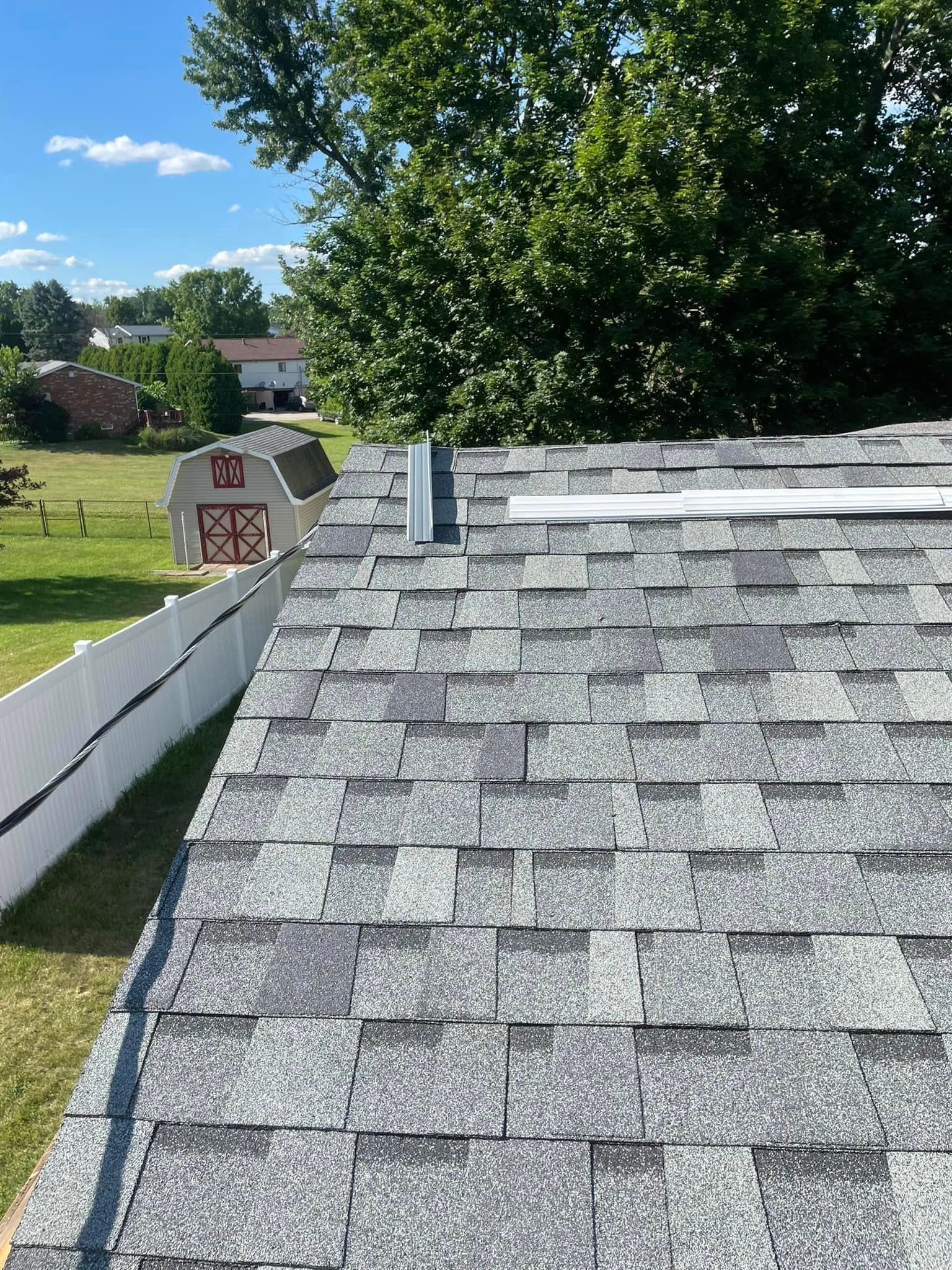 A roof with a chimney on it and a barn in the background.