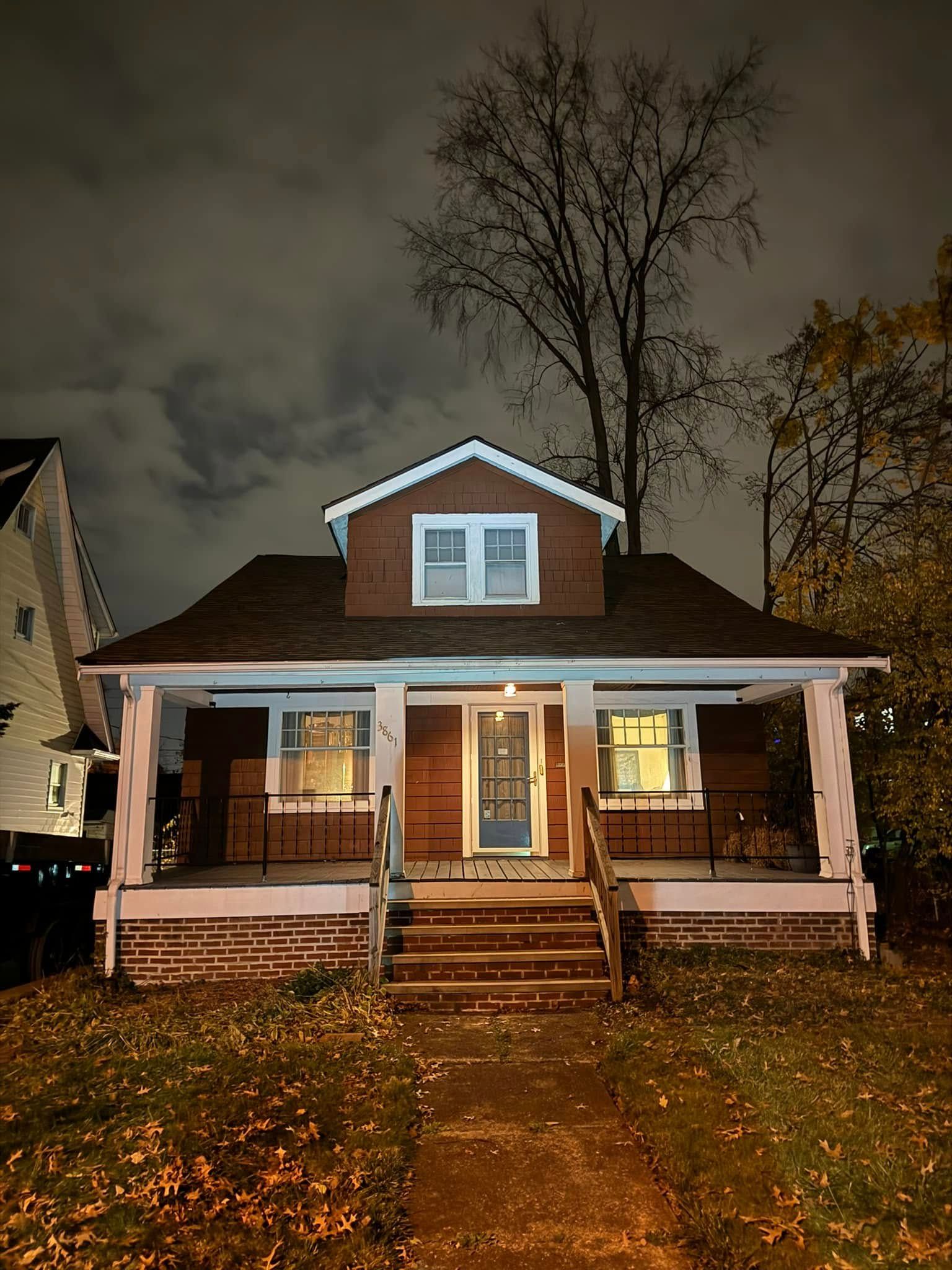 A house is lit up at night with a tree in the background.