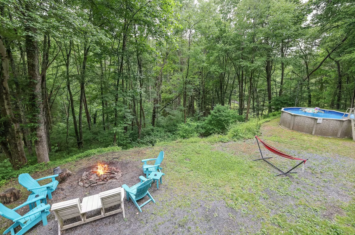A fire pit in the middle of a lush green forest next to a pool.