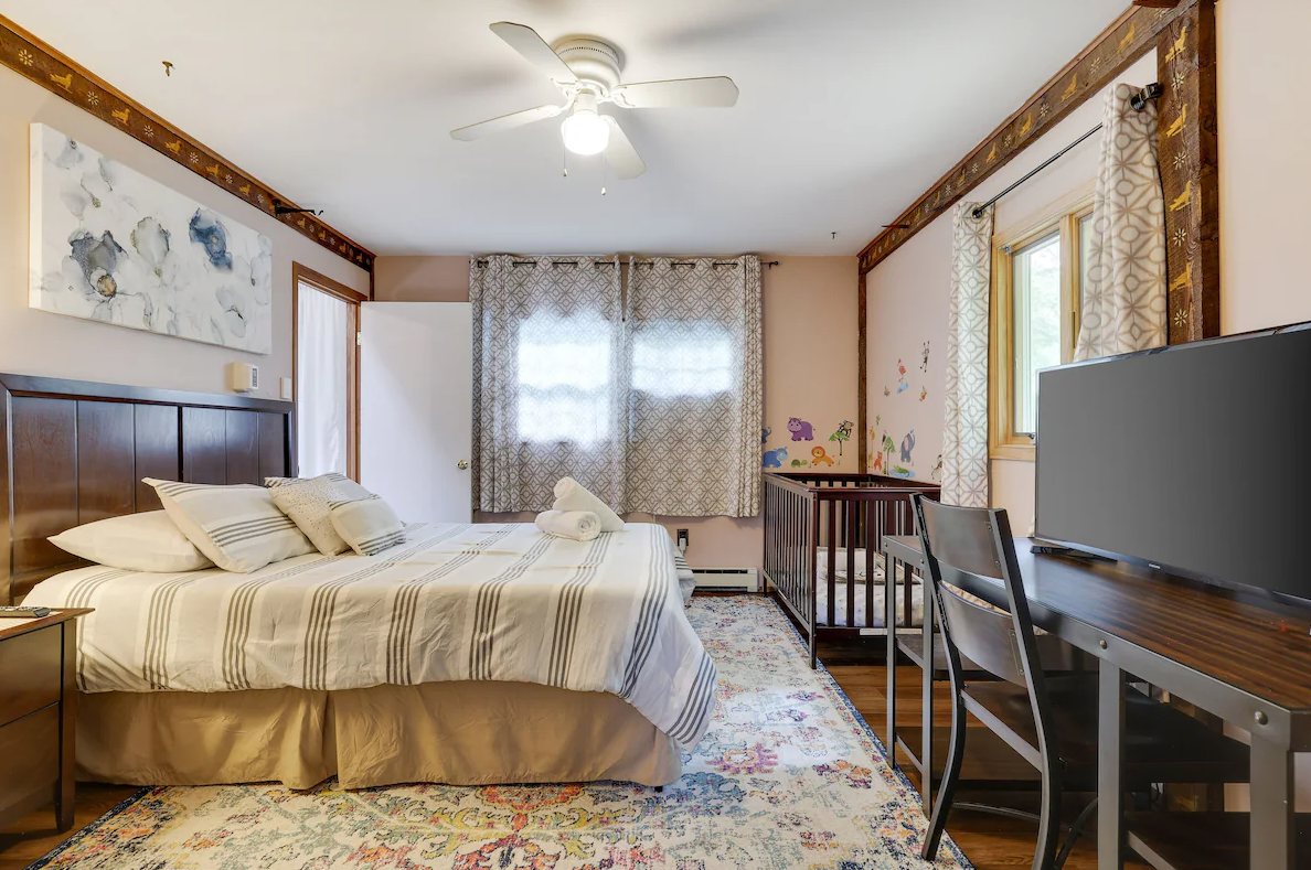 A bedroom with a large bed , a crib , a desk and a television.