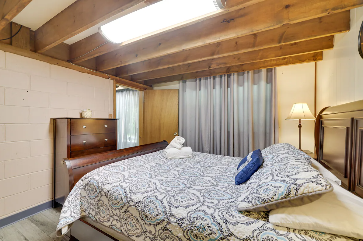 A bedroom with a bed , dresser , lamp and curtains.