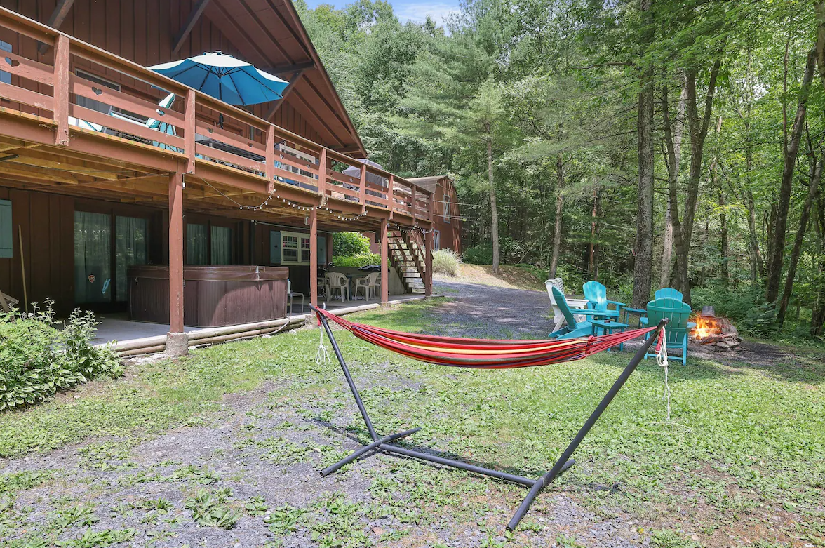 A hammock is sitting in front of a cabin in the woods.