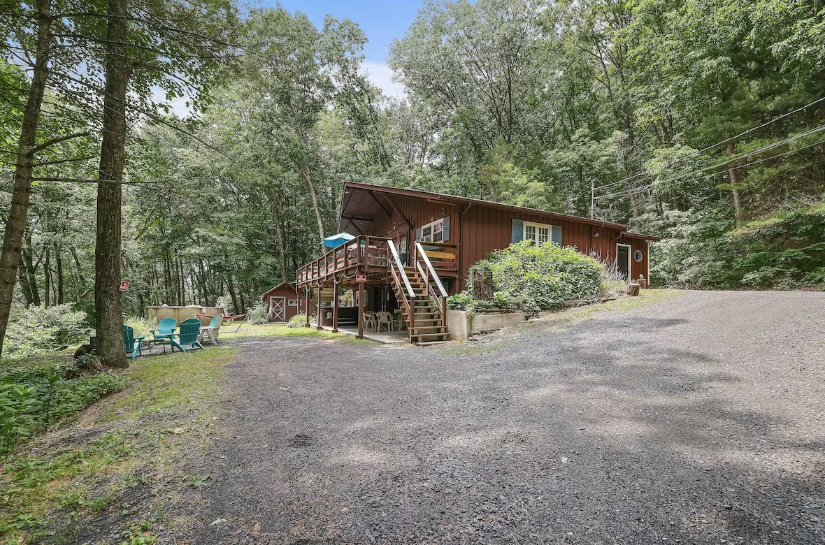 A large red house is surrounded by trees and a gravel driveway.