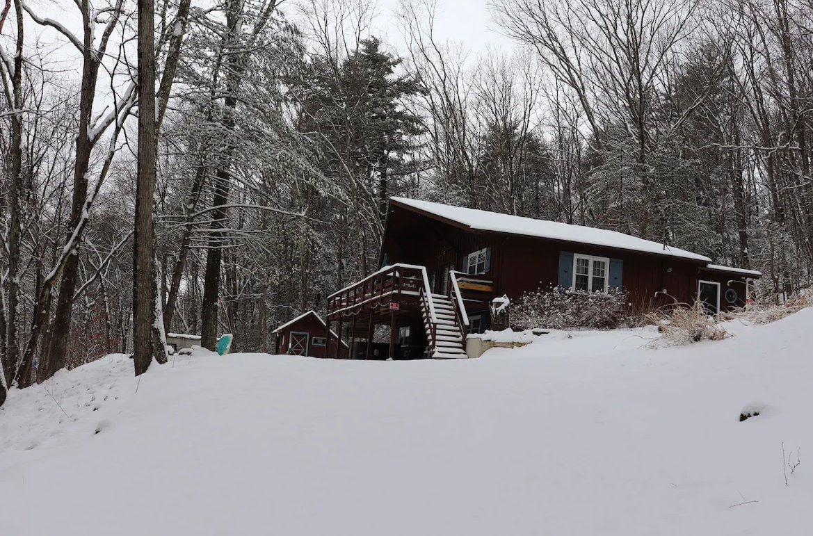 A house in the middle of a snowy forest with trees covered in snow.