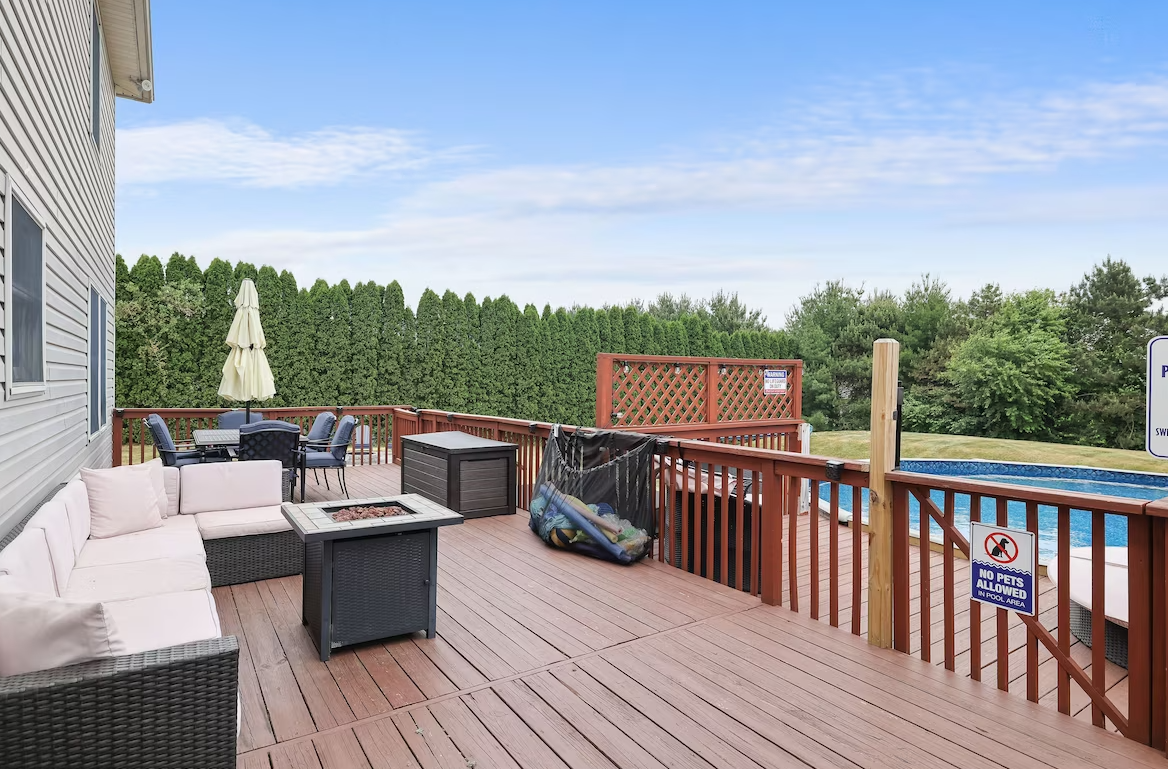 A large deck with a fire pit and a pool in the background