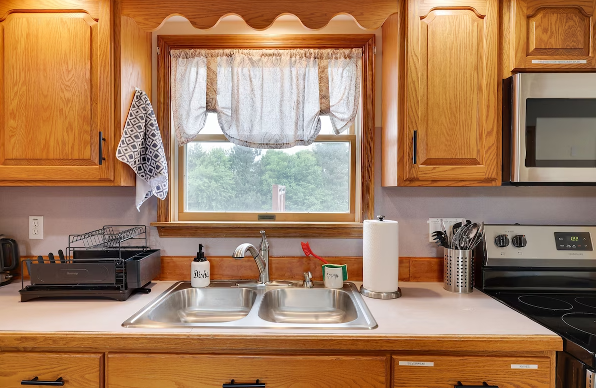 A kitchen with a sink , stove , microwave and window.
