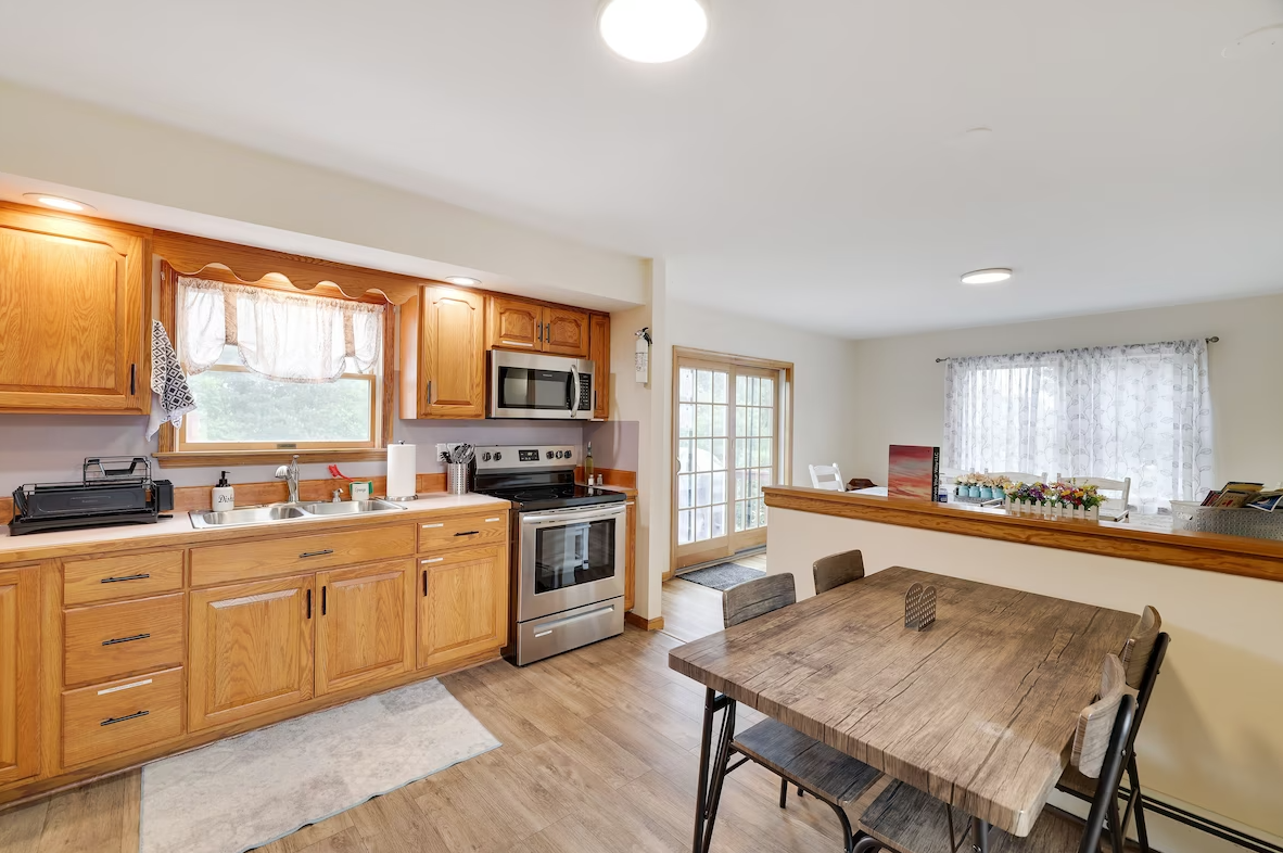 A kitchen with wooden cabinets , stainless steel appliances , a wooden table and chairs.