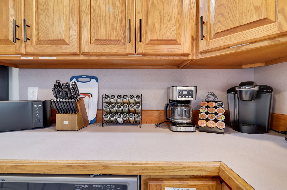A kitchen with wooden cabinets , a coffee maker , a microwave , and a cutting board.