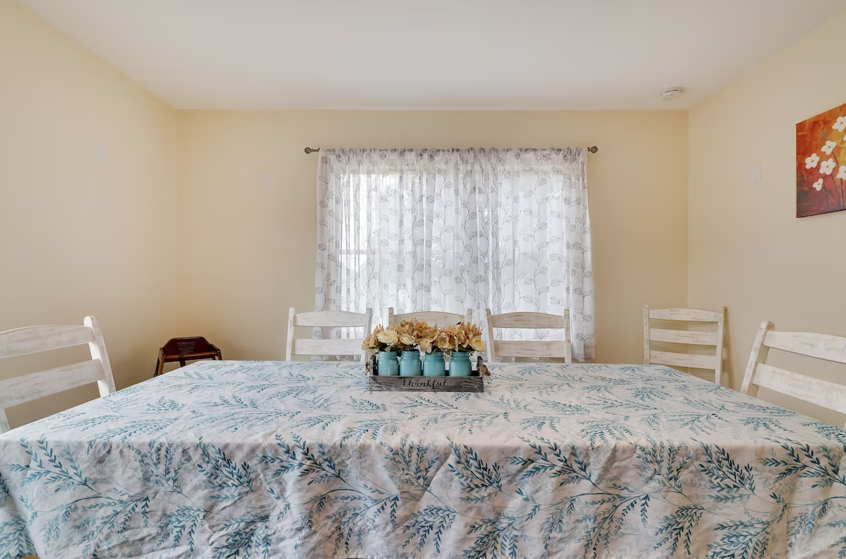 A dining room table with a blue and white tablecloth and white chairs.