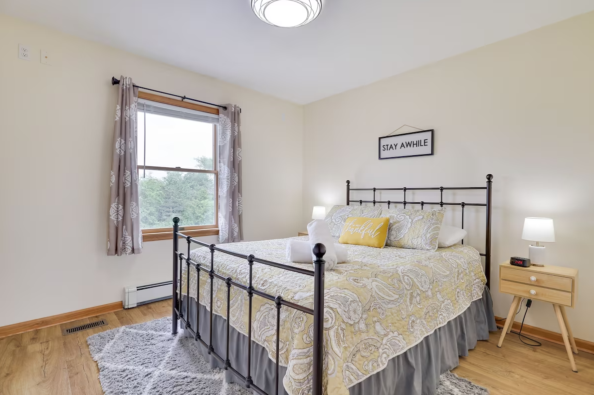 A bedroom with a bed , nightstand , lamp and window.