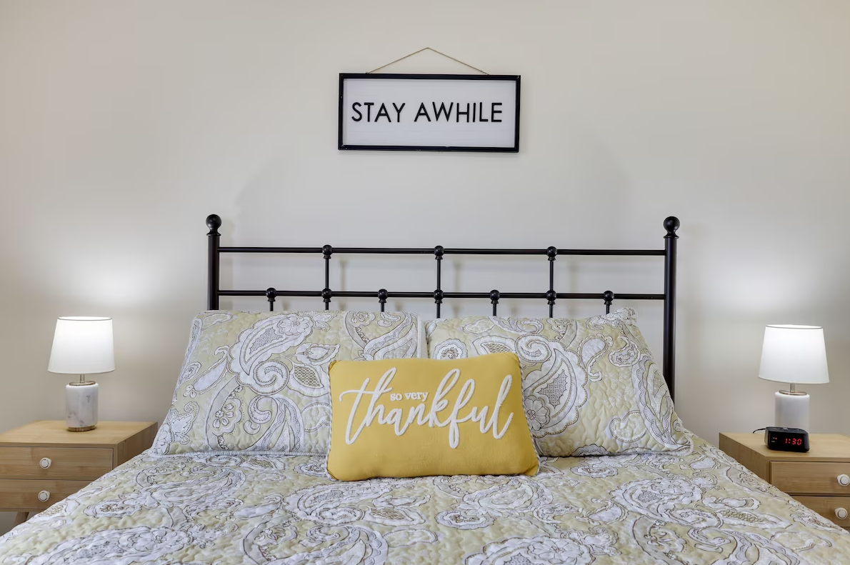 There is a sign above the bed that says `` stay awhile ''.