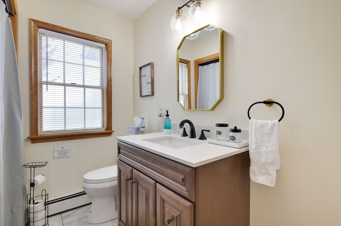 A bathroom with a sink , toilet , mirror and window.