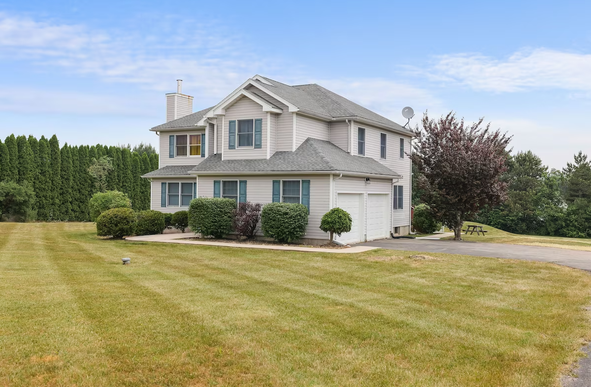 A white house with a gray roof is sitting on top of a lush green field.