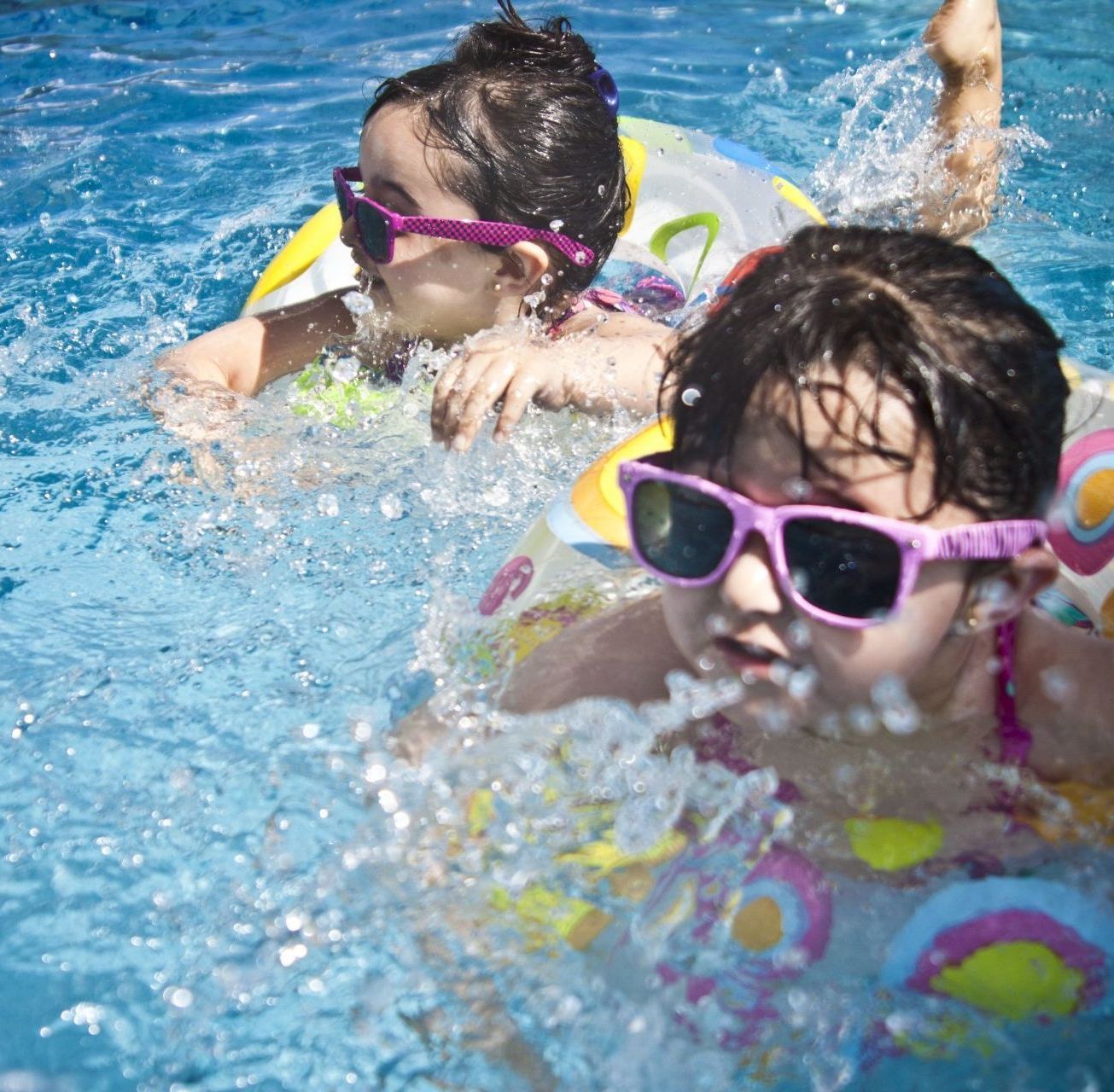 Two children wearing sunglasses are swimming in a pool