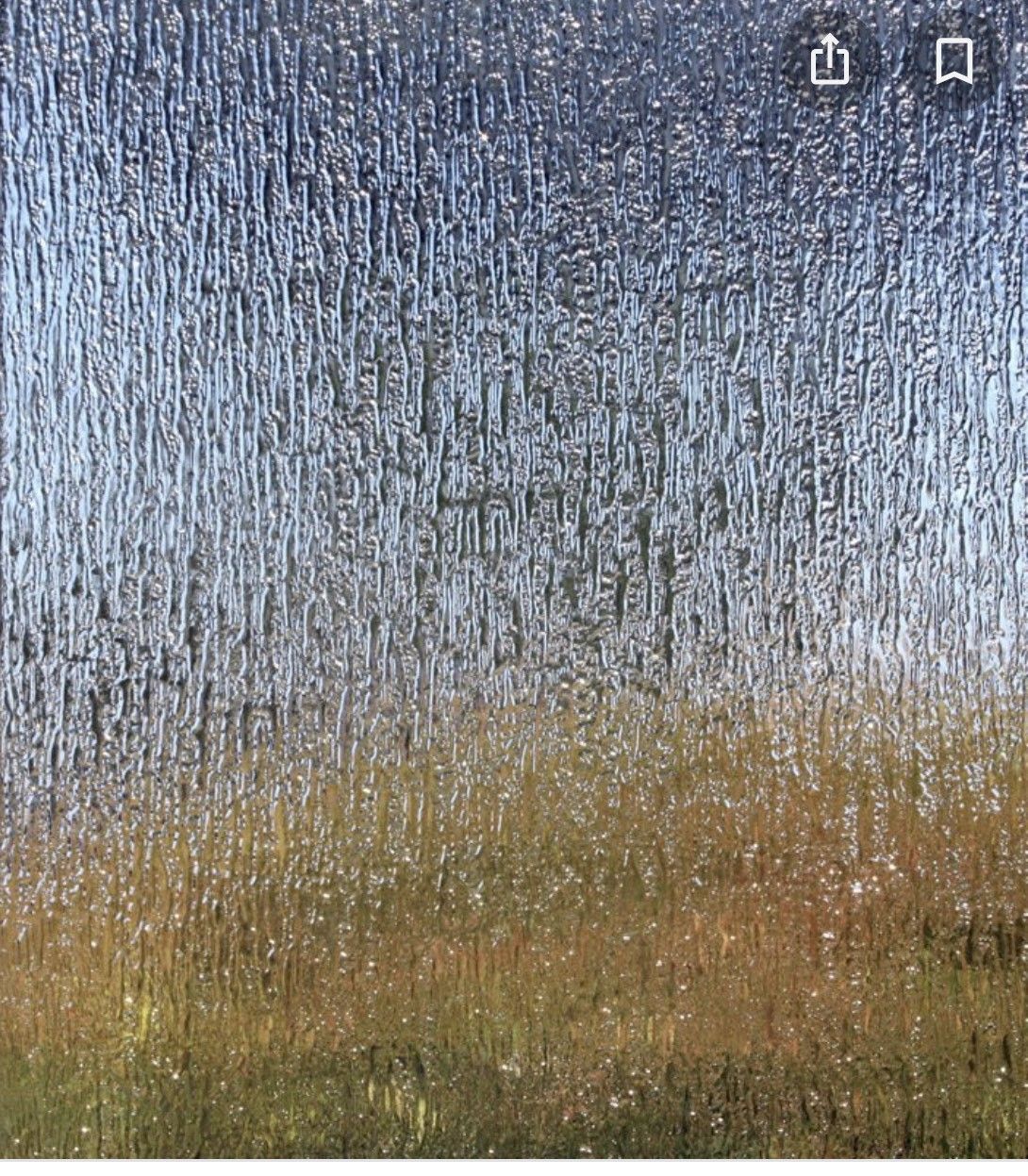 Blurred view through textured glass of blue sky above a brown-green field