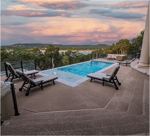 Poolside view at dusk overlooking a lake, with lounge chairs and a colorful sunset sky.