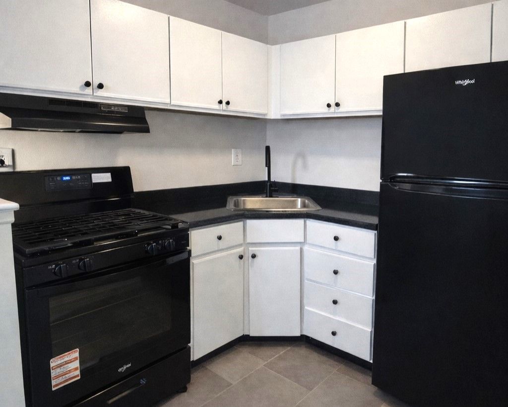 Compact kitchen with black appliances, white cabinets, and dark countertops in an L-shaped layout