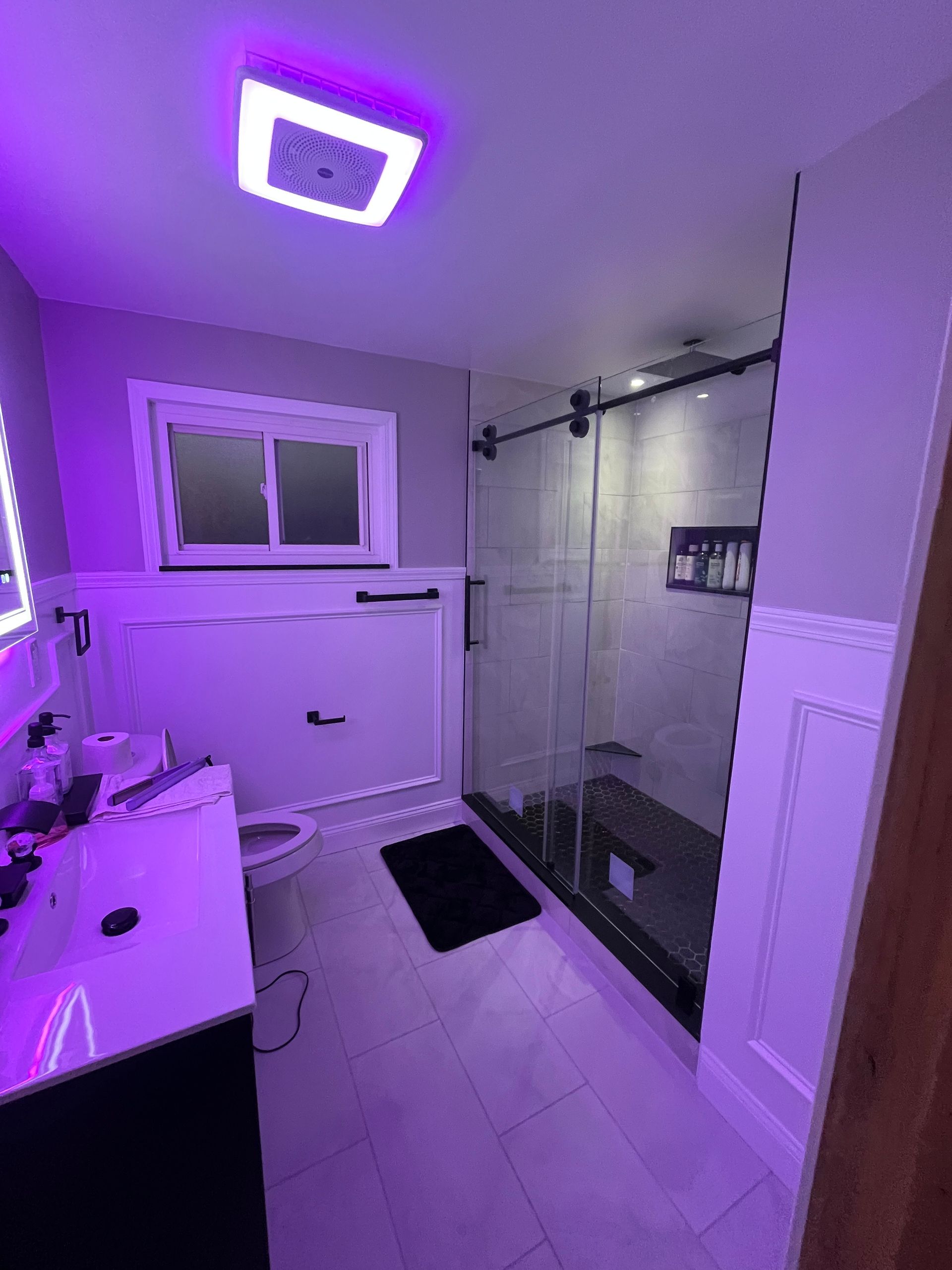 A bathroom with a toilet , sink , shower and purple lights.