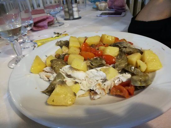 Piatto di cibo: patate, pomodori, carciofi e pesce su una tovaglia bianca.