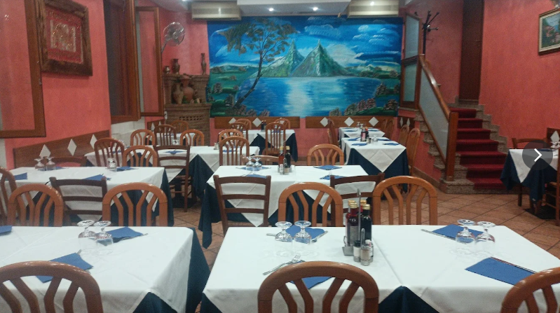 Interno di un ristorante con tavoli apparecchiati per la cena; tovaglie blu e bianche, opere d'arte alle pareti.