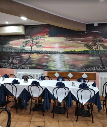 Interno del ristorante con tavoli apparecchiati per cenare e un murale raffigurante un tramonto sull'acqua.
