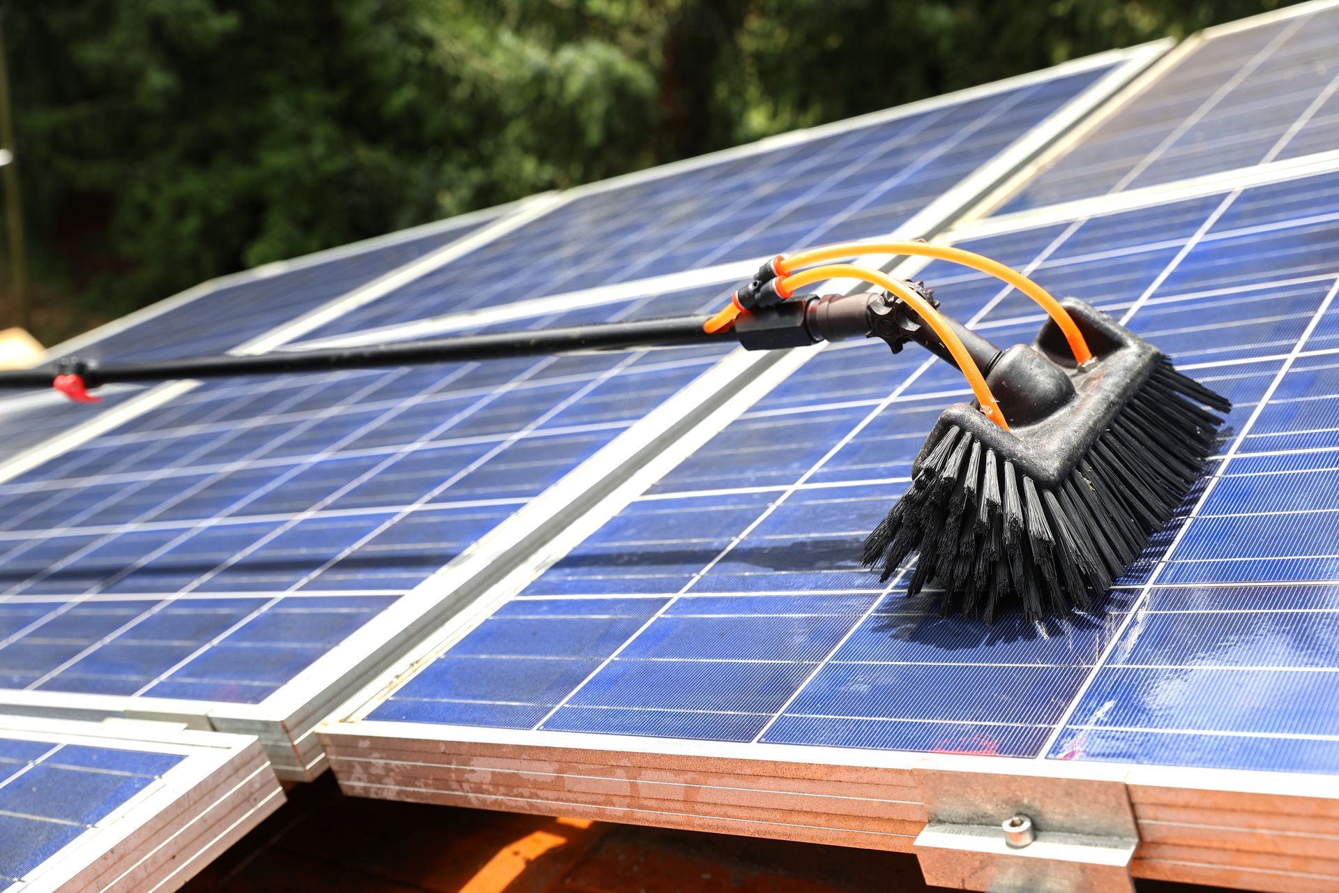 A person wearing a white hard hat and work clothes cleans a solar panel with a squeegee in an outdoor field.
