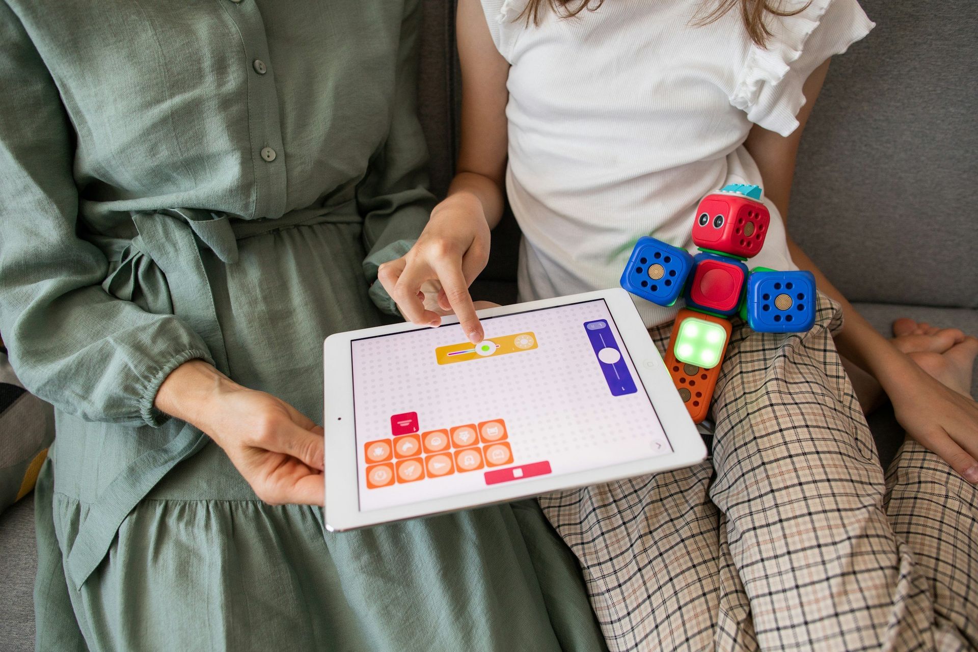 Woman and child code a robot using a tablet. Brightly colored robot on child's leg.