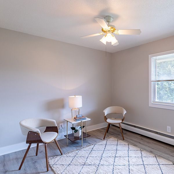 Bright living room corner with two chairs, side table, lamp, patterned rug, and ceiling fan