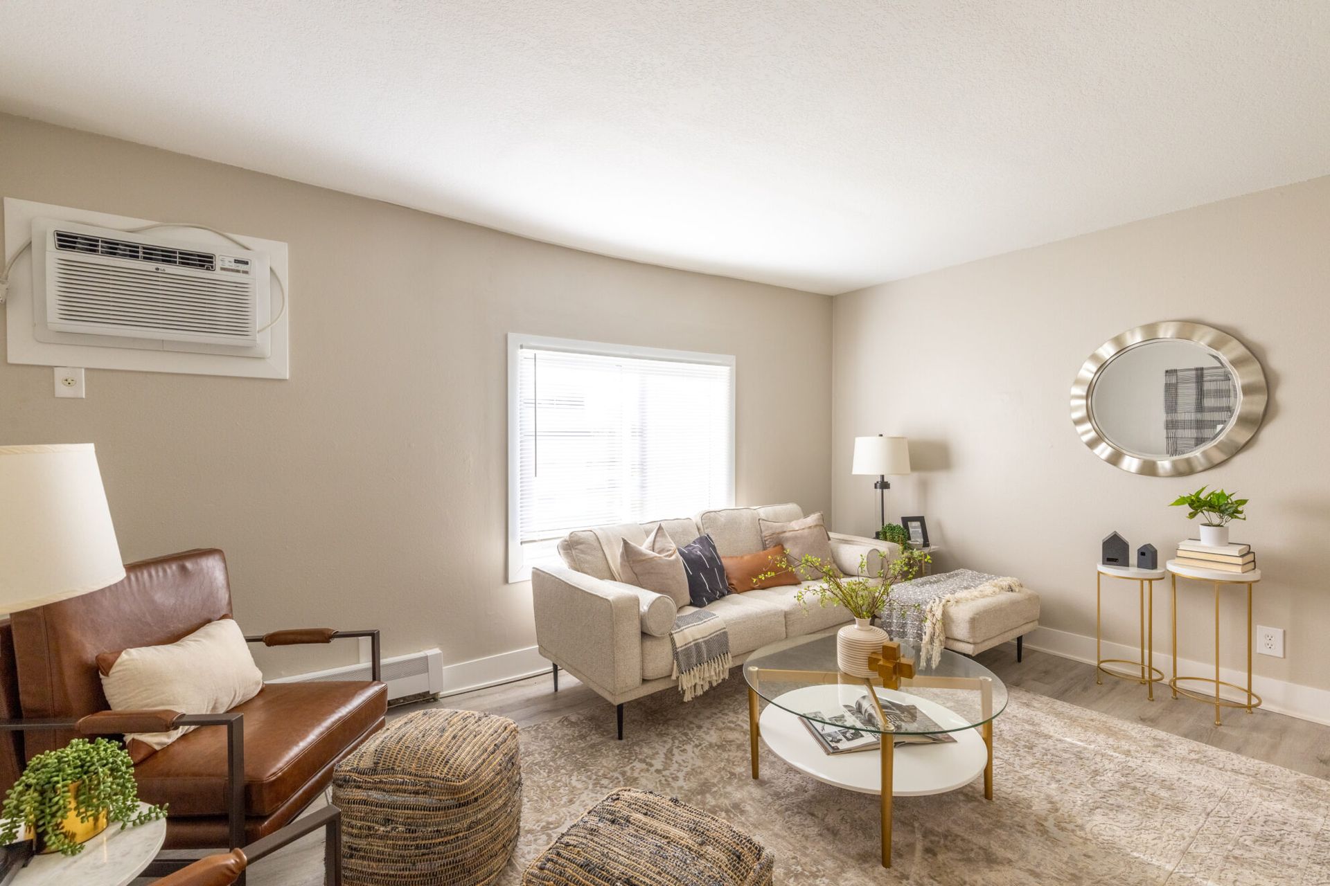 Bright beige living room with sofa, armchair, coffee table, lamp, wall mirror, and window light