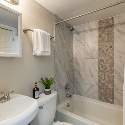 Compact beige bathroom with sink, toilet, bathtub, towel rack, and tiled shower wall