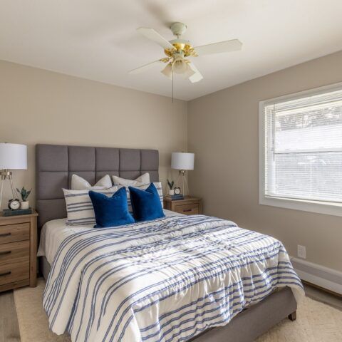 Bedroom with a gray tufted headboard, blue-striped bedding, bedside tables, and a ceiling fan.