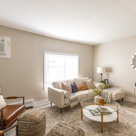 Bright beige living room with sofa, glass coffee table, armchair, lamp, and large window