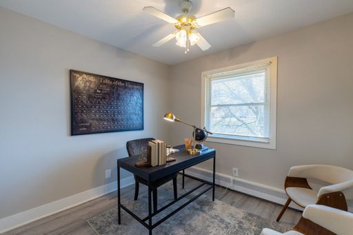 Modern home office with a black desk, wall art, window, ceiling fan, and two beige chairs.