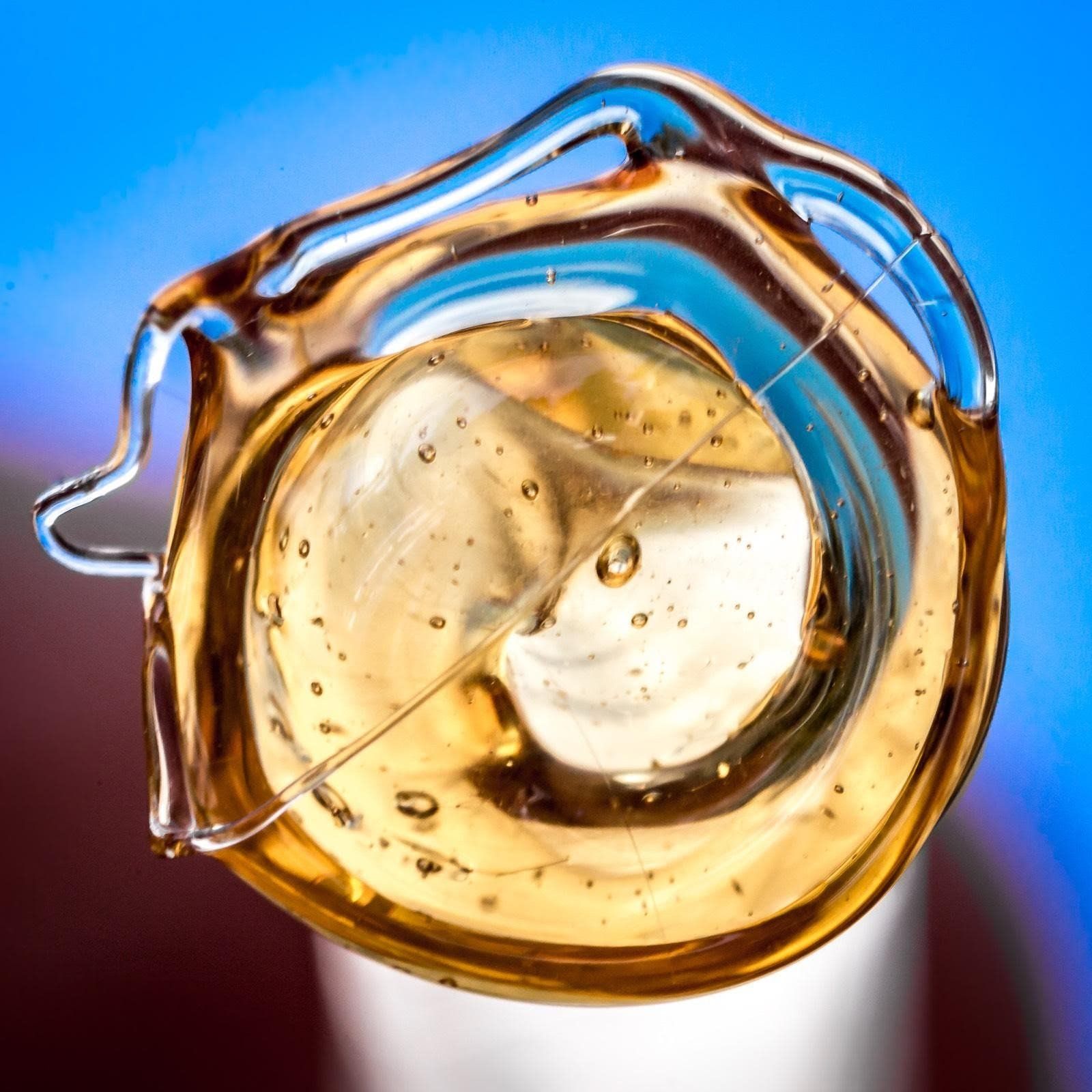 Amber liquid, partially solidified, forming a circular shape with bubbles, against a blue background.