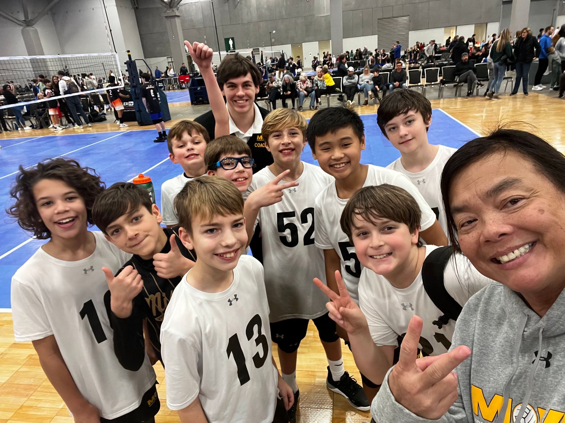 Group of young volleyball players and coach smiling for a selfie on the court.