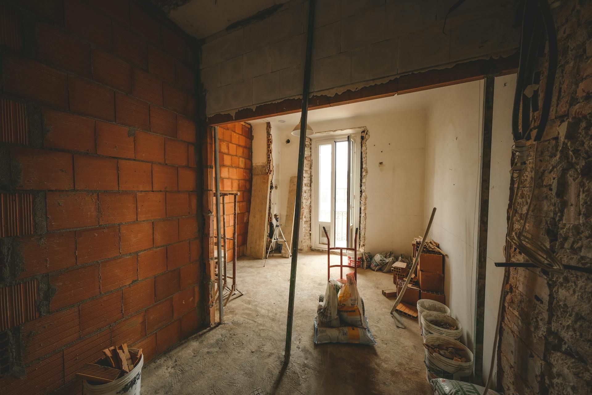 Interior construction site with exposed brick walls and doorway to a room with a window.