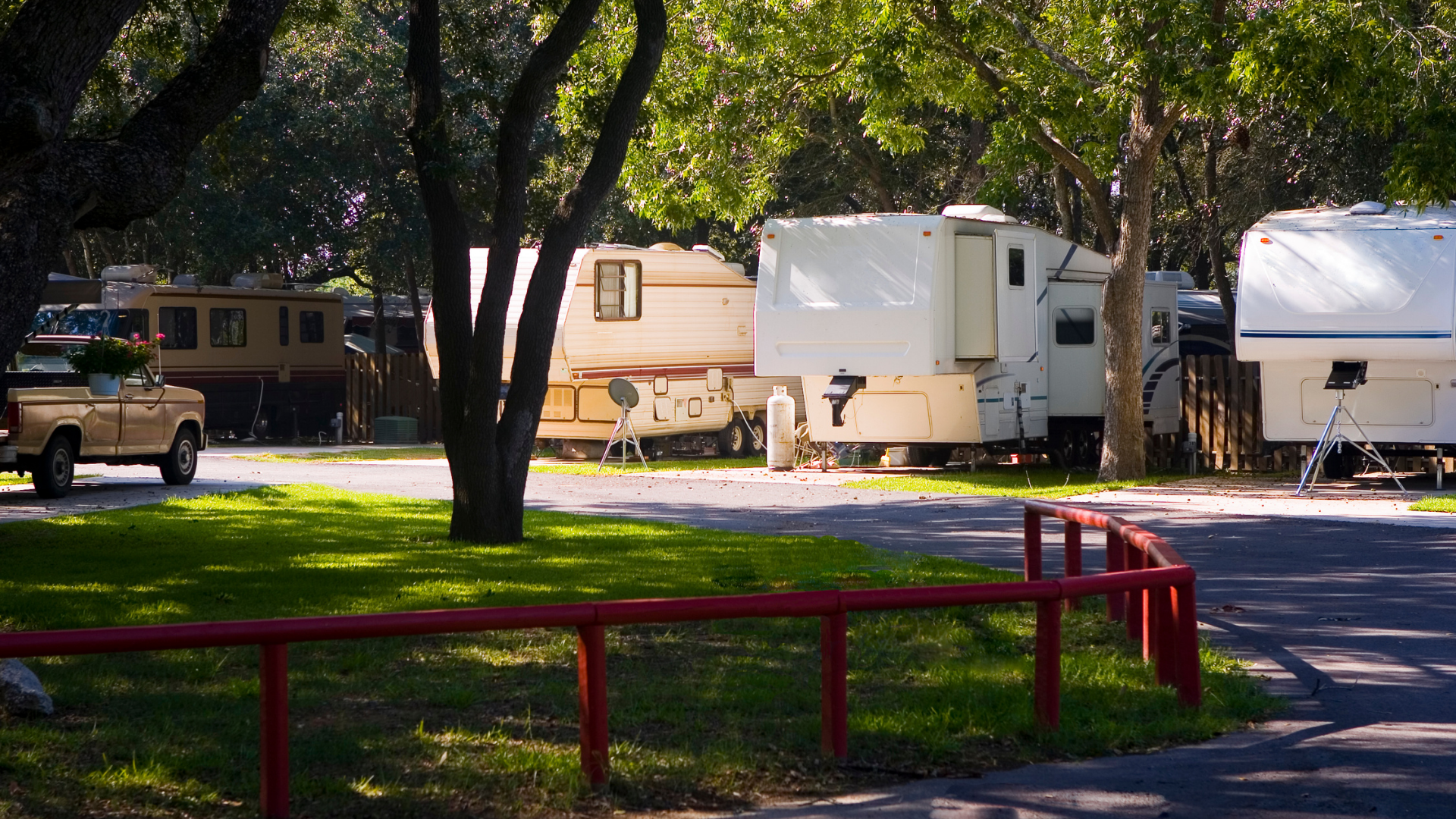 RVs parked in a shaded campsite beside a red metal railing and trees