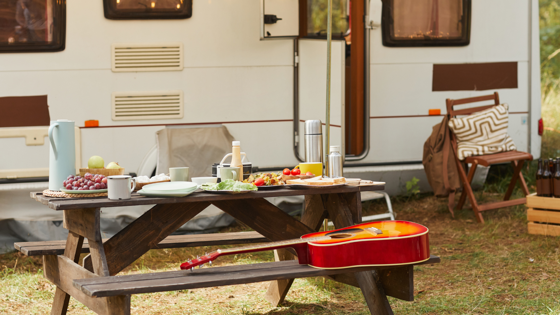 Picnic table with dishes and red cooler outside a camper trailer campsite