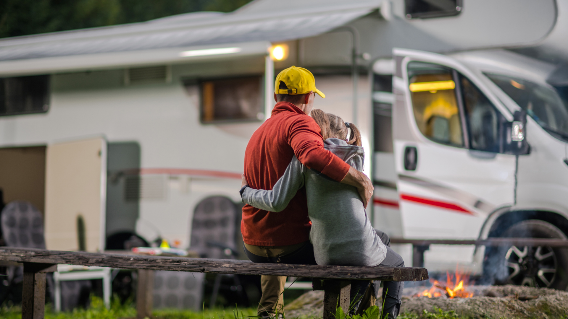 Utility worker in red jacket and yellow helmet sits by a curb with a white truck and smoke in the background