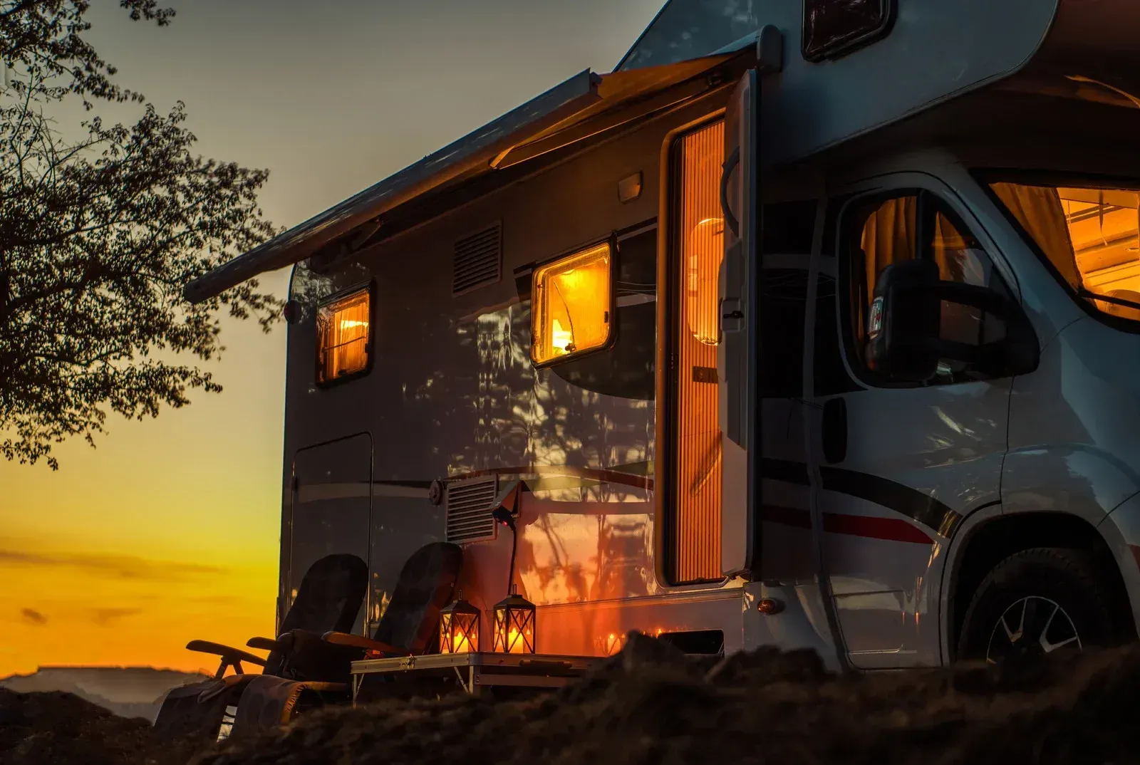 Camper van parked at sunset with warm interior lights and a cozy outdoor setup by the shore
