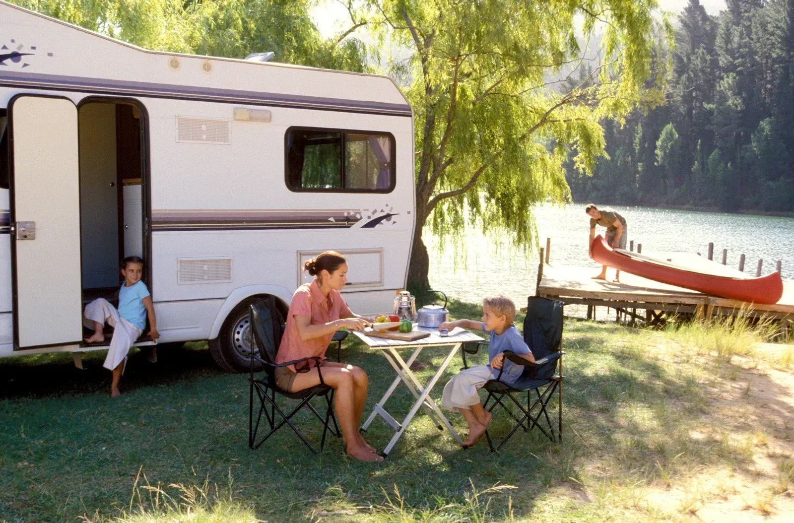 Man fishing from a folding chair beside a calm pond with RVs and trees in the background