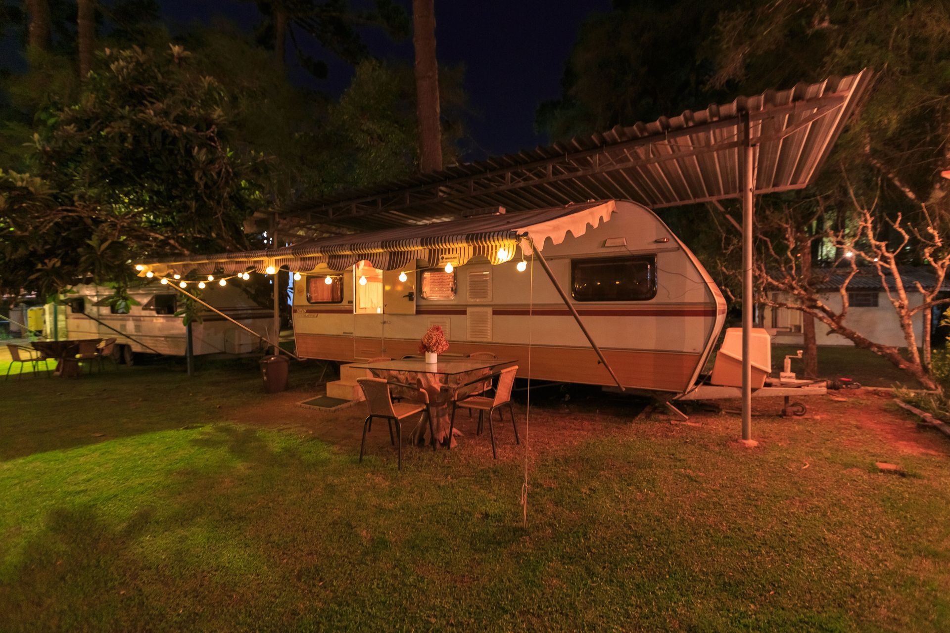 Lit caravan camper with awning and string lights in a grassy yard at night